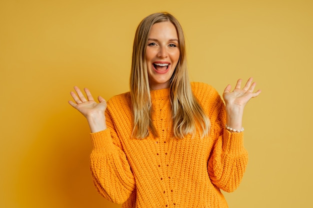 Jolie femme blonde au visage suprice en pull d'automne élégant orange posant sur jaune.