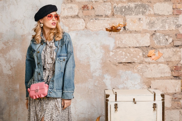 Jolie femme blonde élégante en jeans et veste surdimensionnée posant contre le mur dans la rue