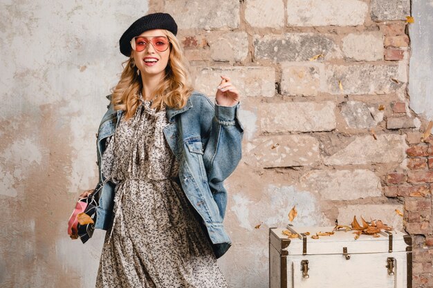 Jolie femme blonde élégante en jeans et veste surdimensionnée posant contre le mur dans la rue