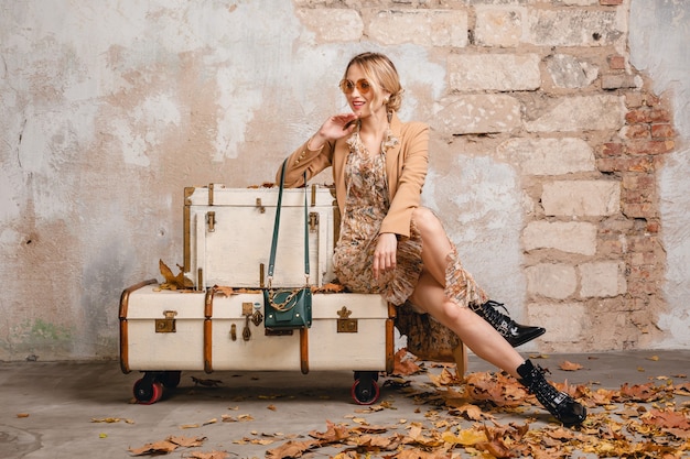 Jolie femme blonde élégante en manteau beige marchant dans la rue contre le mur vintage