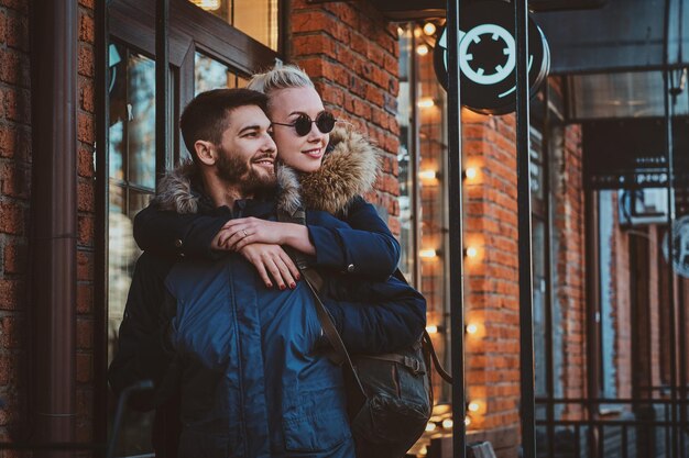 Jolie femme blonde à lunettes de soleil étreint son bel homme dans la rue.