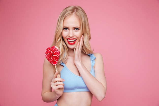 Jolie femme blonde en maillot de bain posant avec une sucette en forme de coeur