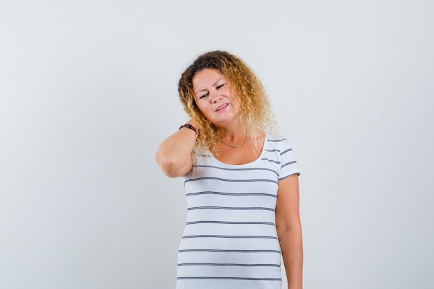 Jolie femme blonde en t-shirt rayé souffrant de douleurs au cou et ayant l'air fatigué, vue de face.