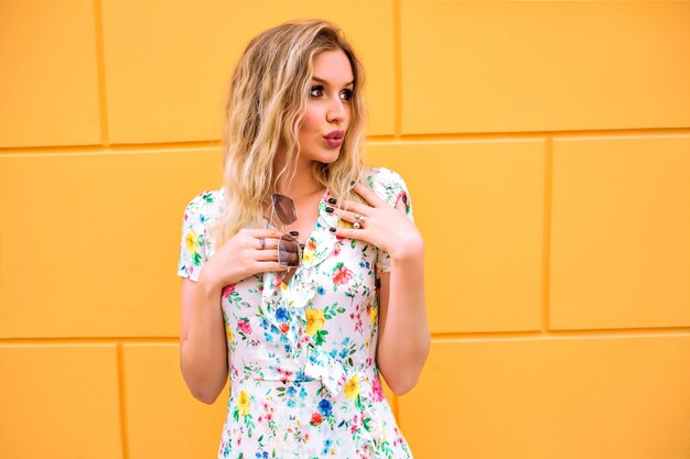 Jolie Femme Blonde Vêtue D'une Robe à Fleurs, Posant Près Du Mur Jaune