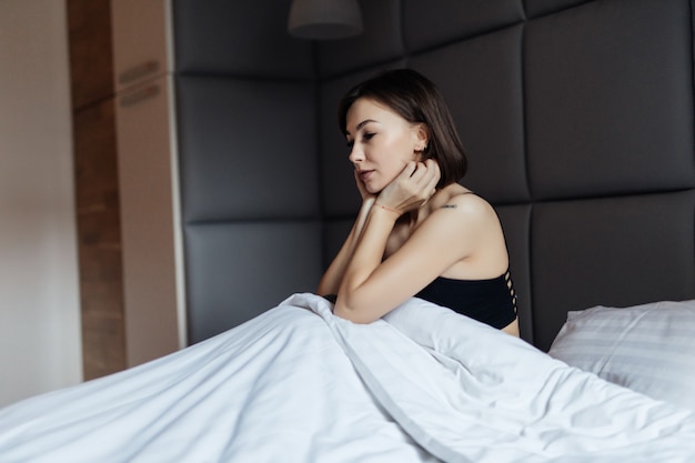 Jolie femme brune cheveux longs sur lit blanc dans une douce lumière du matin sous la couette