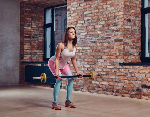 Jolie femme brune faisant des squats avec haltères dans un club avec intérieur loft.