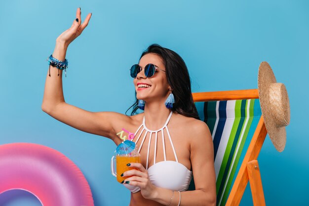 Jolie femme brune à lunettes de soleil en agitant la main avec le sourire