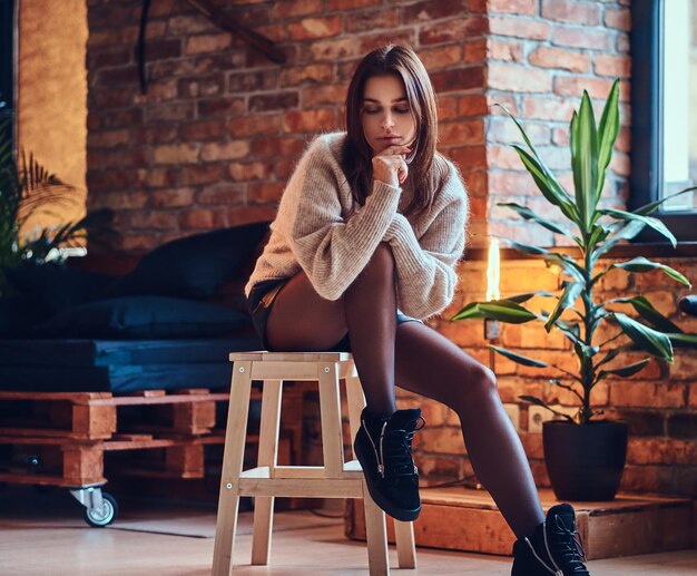 Jolie femme brune posant près de la fenêtre dans une pièce avec intérieur loft.