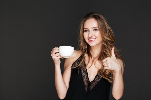 Jolie femme buvant du café et faire le geste du pouce en l'air