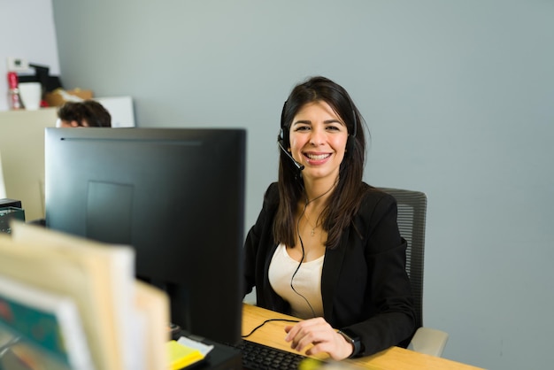 Photo gratuite jolie femme avec un casque assis sur un centre d'appels et se sentant heureuse tout en recevant des appels. cadre féminin travaillant en tant que représentant des ventes