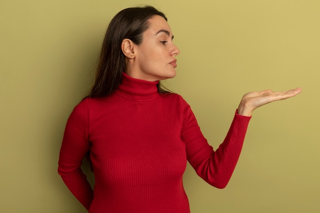 Jolie femme caucasienne confiante regarde et tient la main ouverte sur vert olive