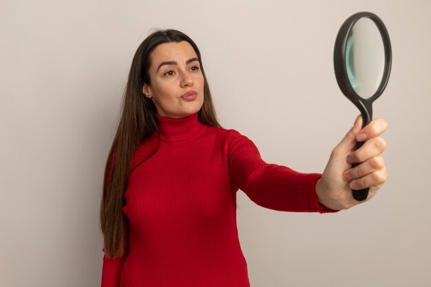 Jolie femme caucasienne confiante tient et regarde la loupe isolée