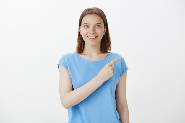 Jolie femme caucasienne pointant dans le coin supérieur droit et souriant, invitant à vérifier l'offre promotionnelle, bannière de réduction spéciale