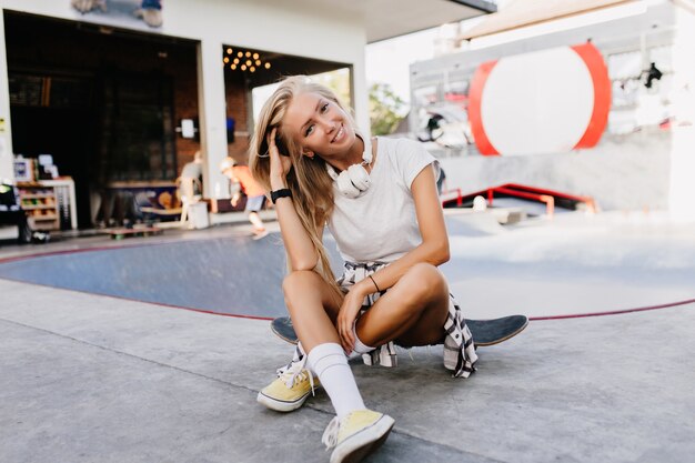 Jolie femme caucasienne posant avec plaisir dans le skate park. Jolie jeune femme blonde assise sur une planche à roulettes et souriant.