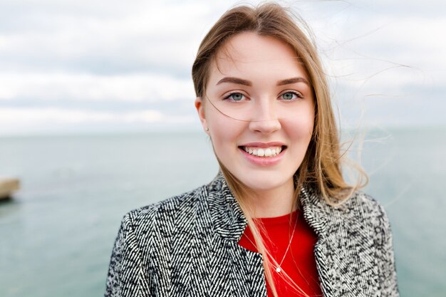 Jolie femme charmante avec de longs cheveux brun clair et de grands yeux bleus sourit à l'extérieur