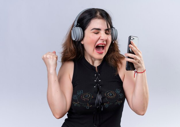 Jolie femme en chemisier noir tenant le téléphone, écouter de la musique avec des écouteurs et danser