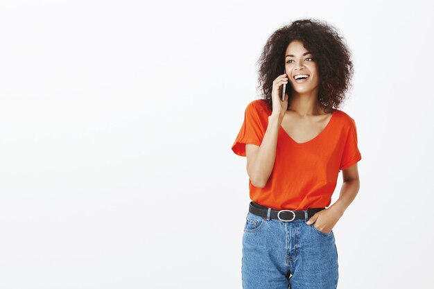 Jolie femme avec une coiffure afro posant avec son smartphone en studio