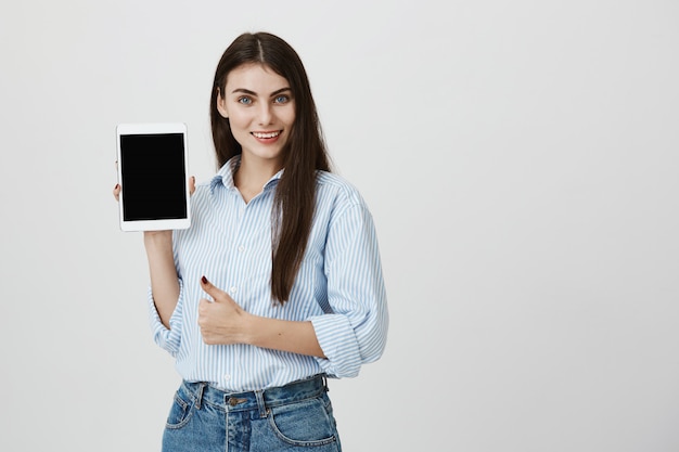 Jolie femme confiante pouce en l'air comme montrant l'écran de la tablette numérique