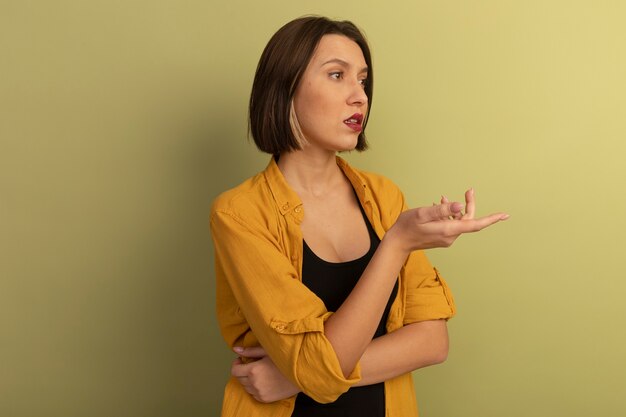 Jolie femme confiante regarde et pointe sur le côté isolé sur mur vert olive