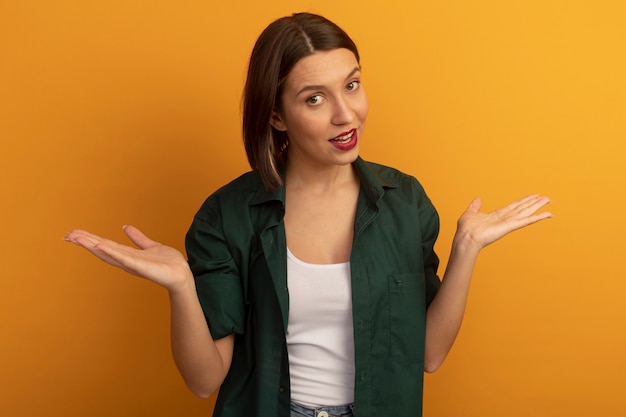 Jolie femme confiante tient les mains ouvertes isolé sur mur orange