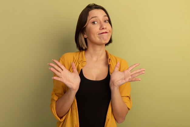 Jolie femme confuse se tient avec les mains surélevées isolé sur mur vert olive
