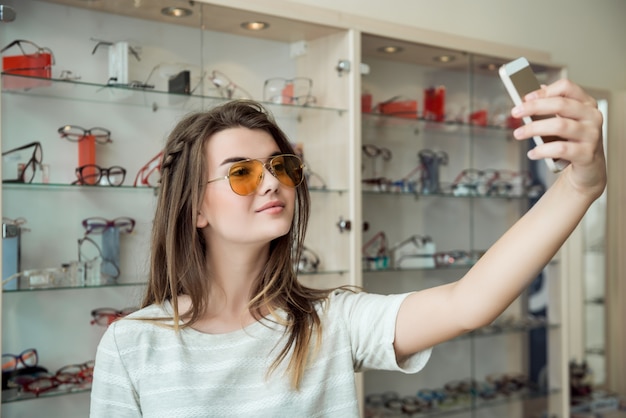 Jolie femme a continué à faire du shopping seule, faisant des selfies tout en essayant de nouvelles lunettes de soleil élégantes dans une boutique d'opticien, envoyant une photo à un ami