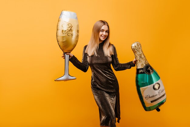 Jolie femme dansant sur orange avec une bouteille de champagne. Portrait intérieur de femme caucasienne jocund célébrant son anniversaire avec du vin.