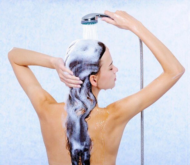 Jolie femme debout en arrière et laver ses longs cheveux