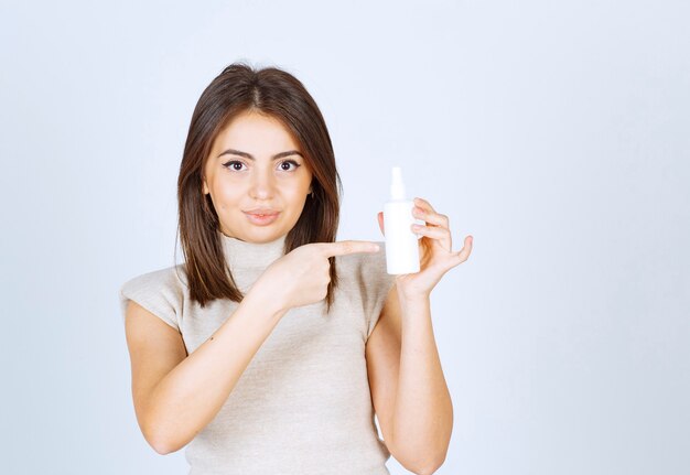 Jolie femme debout et pointant sur un spray sur fond blanc.