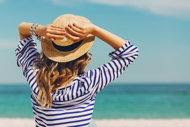 Photo gratuite jolie femme élégante blonde bronzage mince en chapeau de paille et lunettes de soleil, posant sur la plage tropicale paradisiaque