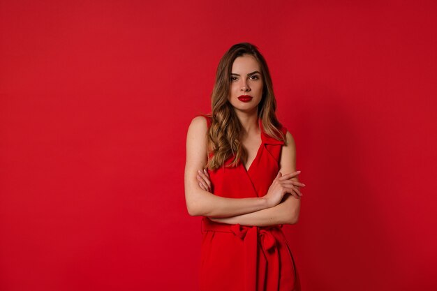 Jolie femme élégante et élégante aux cheveux ondulés, vêtue d'une robe rouge avec du rouge à lèvres rouge