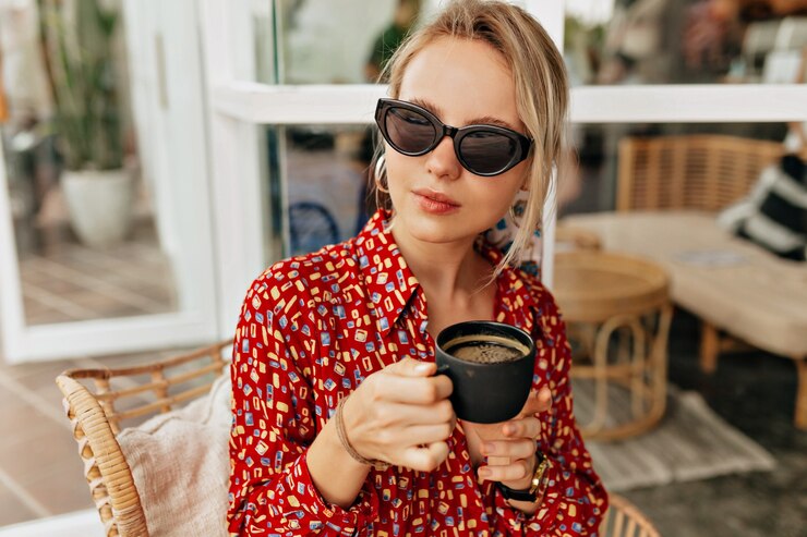 Jolie femme élégante élégante vêtue d'une robe lumineuse, buvant du café et se reposant en plein air