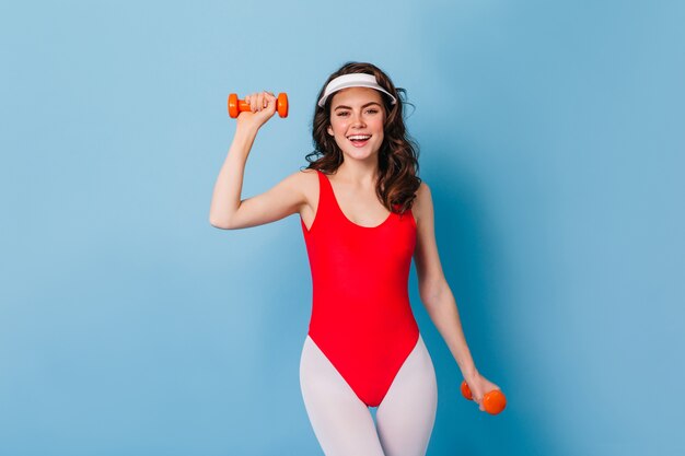 Jolie femme entraîneur de fitness en bonnet blanc et leggings dans le style des années 80 montre un exercice efficace pour les mains