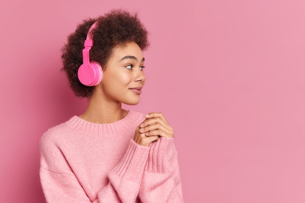 Jolie femme ethnique aux cheveux bouclés porte des écouteurs stéréo sur les oreilles concentrées de côté avec intérêt écoute la musique cavalier occasionnel