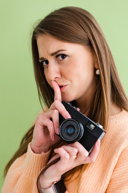 Jolie femme européenne avec appareil photo dans les mains montre positive signe chut avec le doigt, geste de silence