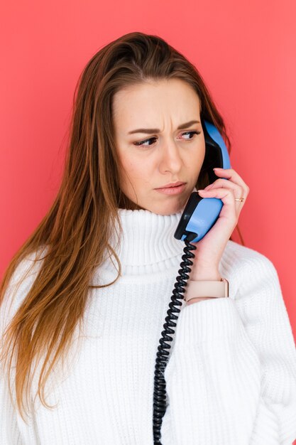 Jolie femme européenne en pull blanc décontracté tenir le téléphone fixe ayant une conversation avec curieux visage sérieux confus