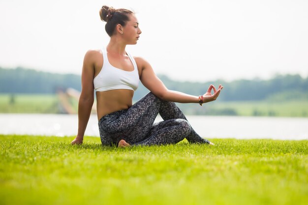 Jolie femme faisant des exercices de yoga dans le parc verdoyant