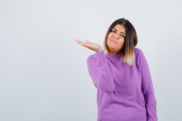 Jolie femme faisant semblant de tenir quelque chose dans un pull violet et ayant l'air confiante, vue de face.