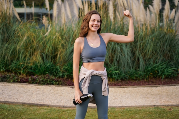 Jolie femme en forme souriante montrant des biceps au parc de la ville