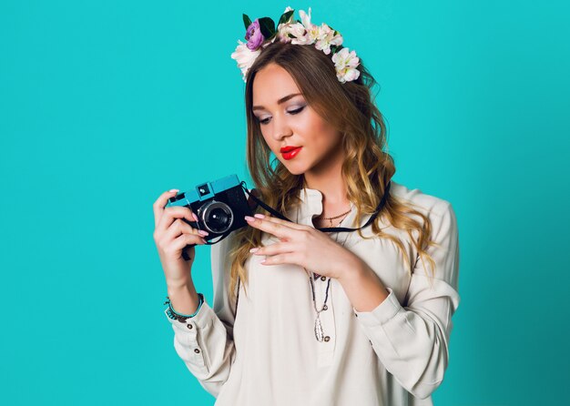 Jolie femme fraîche blonde joyeuse avec une couronne de fleurs sur la tête posant au printemps tenue élégante prenant une photo sur fond bleu clair.Portant une couronne de fleurs tendre, vêtements de printemps.