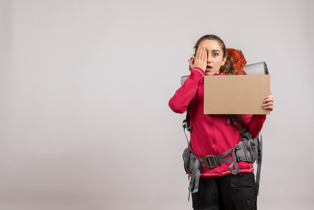 jolie femme avec un gros sac à dos tenant un carton mettant la main sur son œil