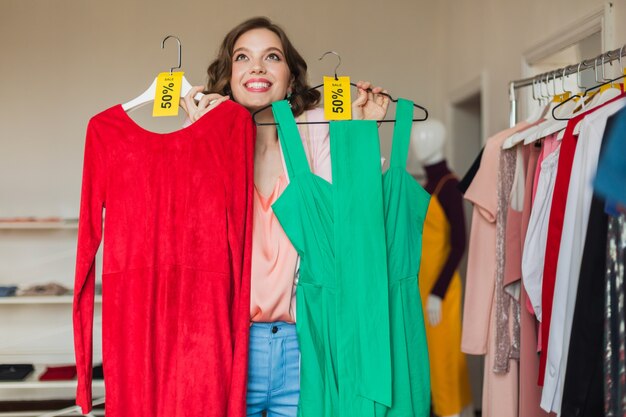 Jolie femme heureuse émotionnelle tenant des robes colorées dans un magasin de vêtements