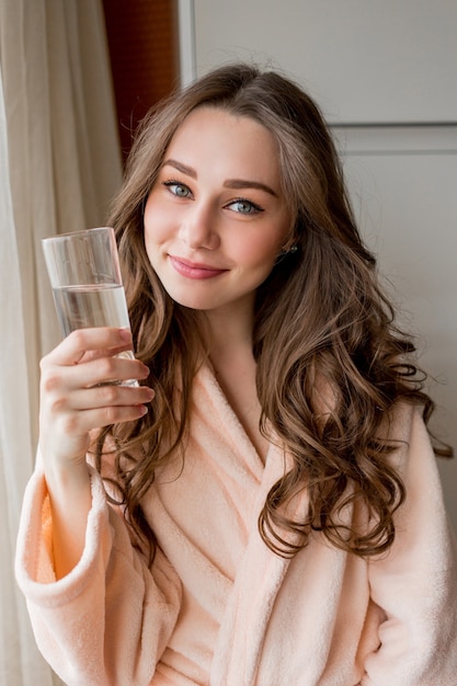 Jolie femme heureuse en peignoir, boire de l'eau fraîche à la maison