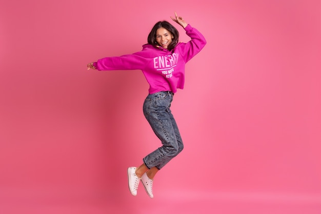 Jolie Femme Hispanique En Sweat à Capuche Rose Et Jeans Souriant Sautant Sur Rose