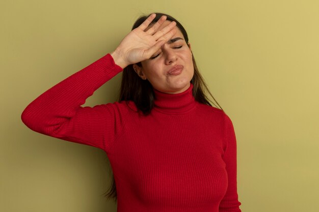 Jolie femme insatisfaite met la main sur le front isolé sur mur vert olive