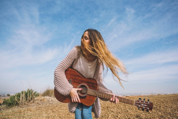 Jolie femme jouant de la guitare dans le champ
