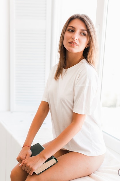 Jolie femme avec livre assis près de la fenêtre