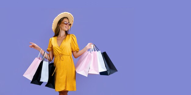 Jolie femme à lunettes de soleil et chapeau détient des sacs colorés sur fond violet concept de vente