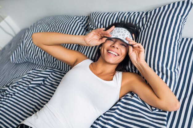 Jolie femme maigre souriante en pyjama couché dans son lit à la maison ayant du repos se réveiller le matin