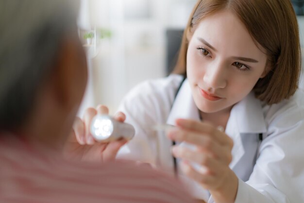 Jolie femme médecin asiatique vérifiant le système du corps de la gorge de la langue d'un patient asiatique âgé à l'hôpital de la clinique